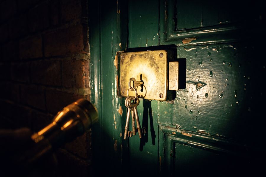 A brass rim lock on a dark wooden door of an older brick building, lit by a handheld flashlight